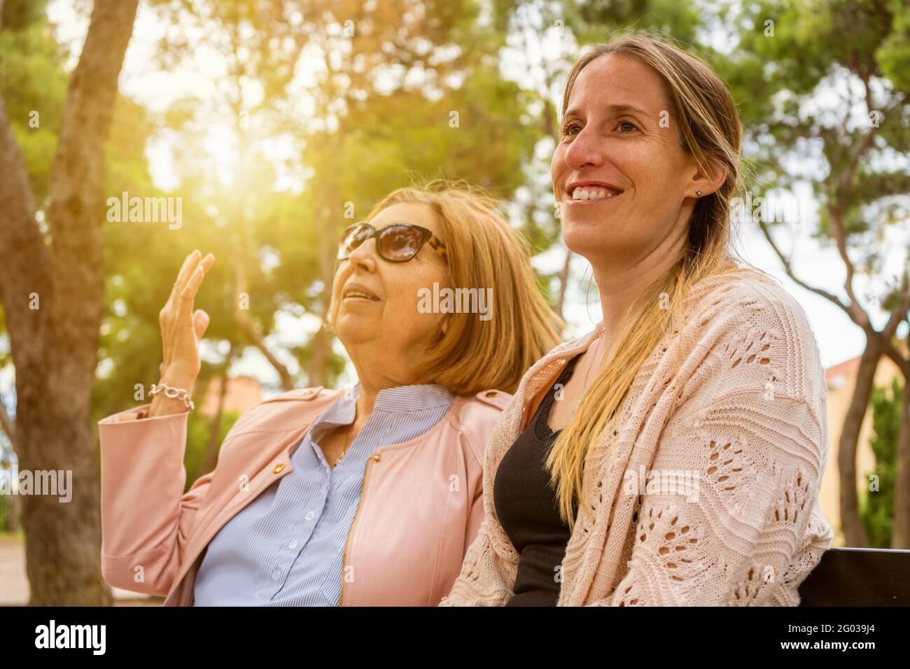 Happy family having fun on weekend.Elderly mother and her adult daughter talking and enjoy time together in nature park at sunset. Stock Photo