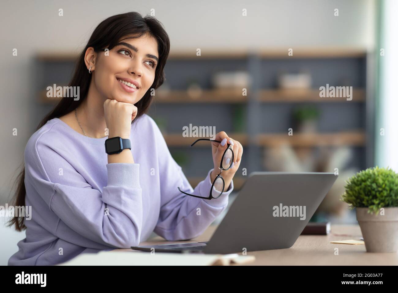 Portrait of smiling young woman sitting at desk adn thinking Stock Photo