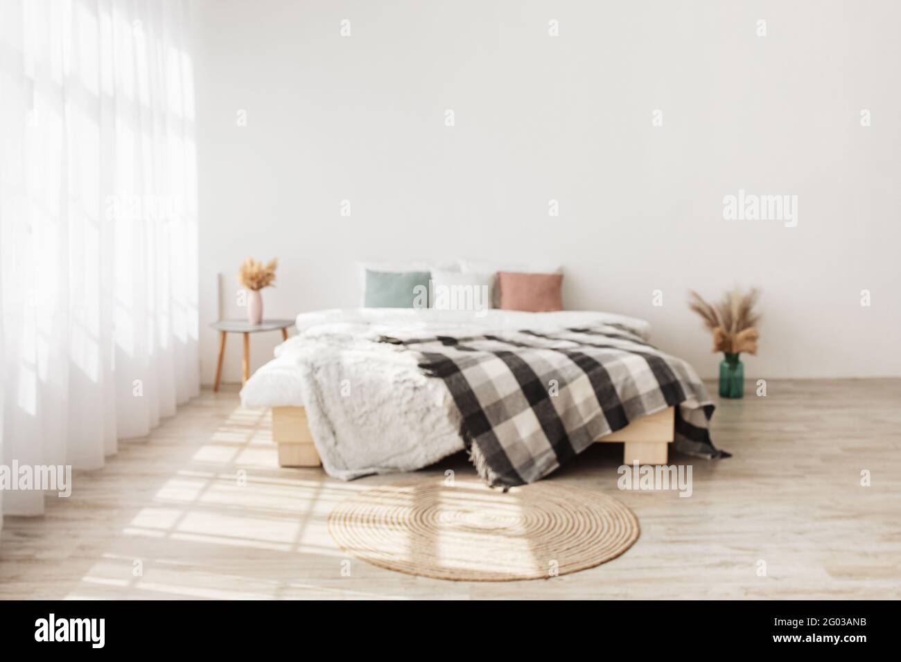 Contemporary boho design in minimalist. Bed with pillows and blanket, table with dry plants in vases Stock Photo