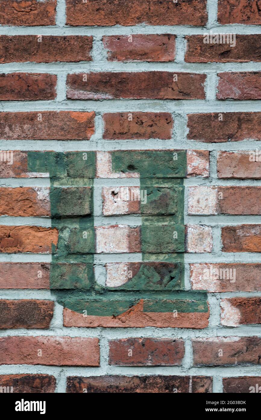 A green letter u painted on a red brick wall Stock Photo