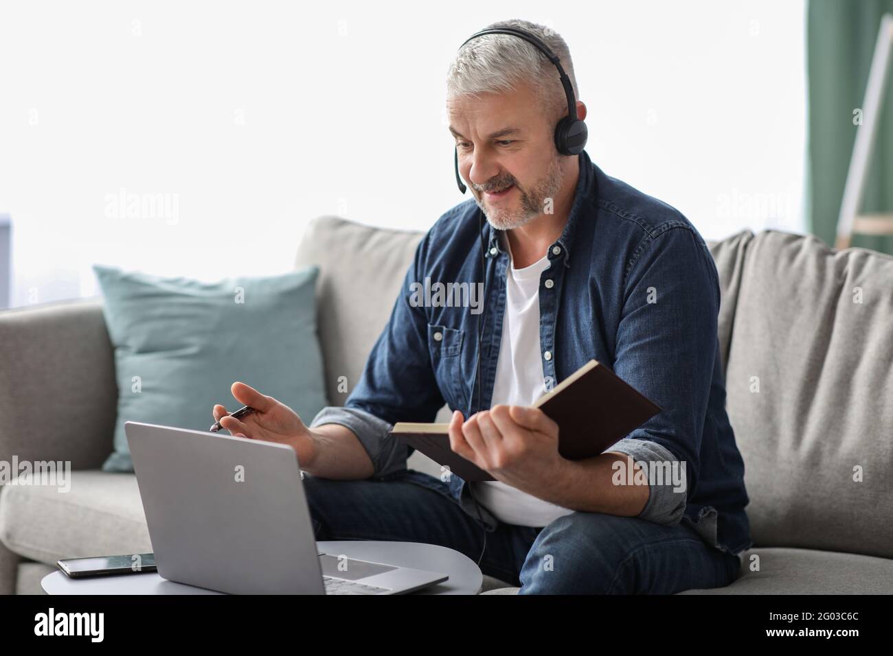 Happy old man having online class, using laptop and headset Stock Photo