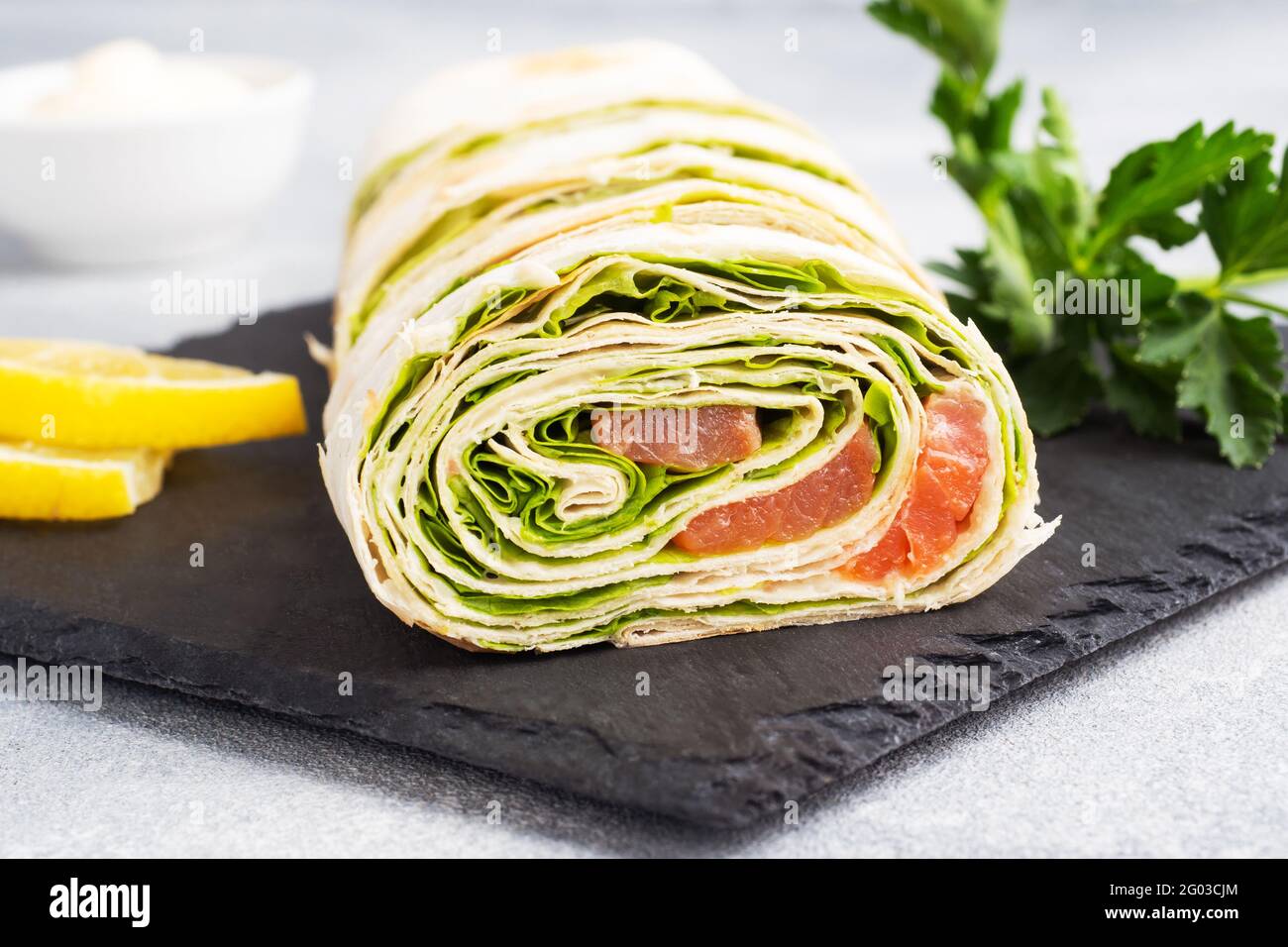 Rolls of thin pita bread and red salted salmon with lettuce leaves On a slate stand, grey concrete background. Copy space Stock Photo