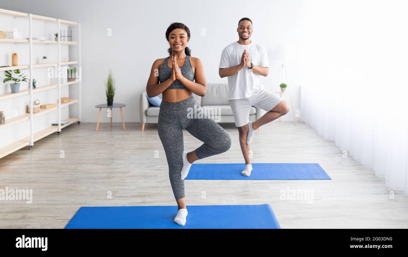 Balance yoga poses. Positive black couple standing in tree asana on sports mats, having morning practice at home Stock Photo