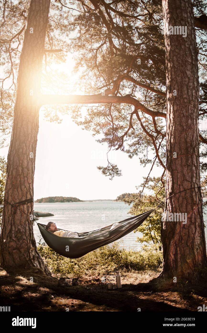 Man sleeping in hammock at lakeshore Stock Photo