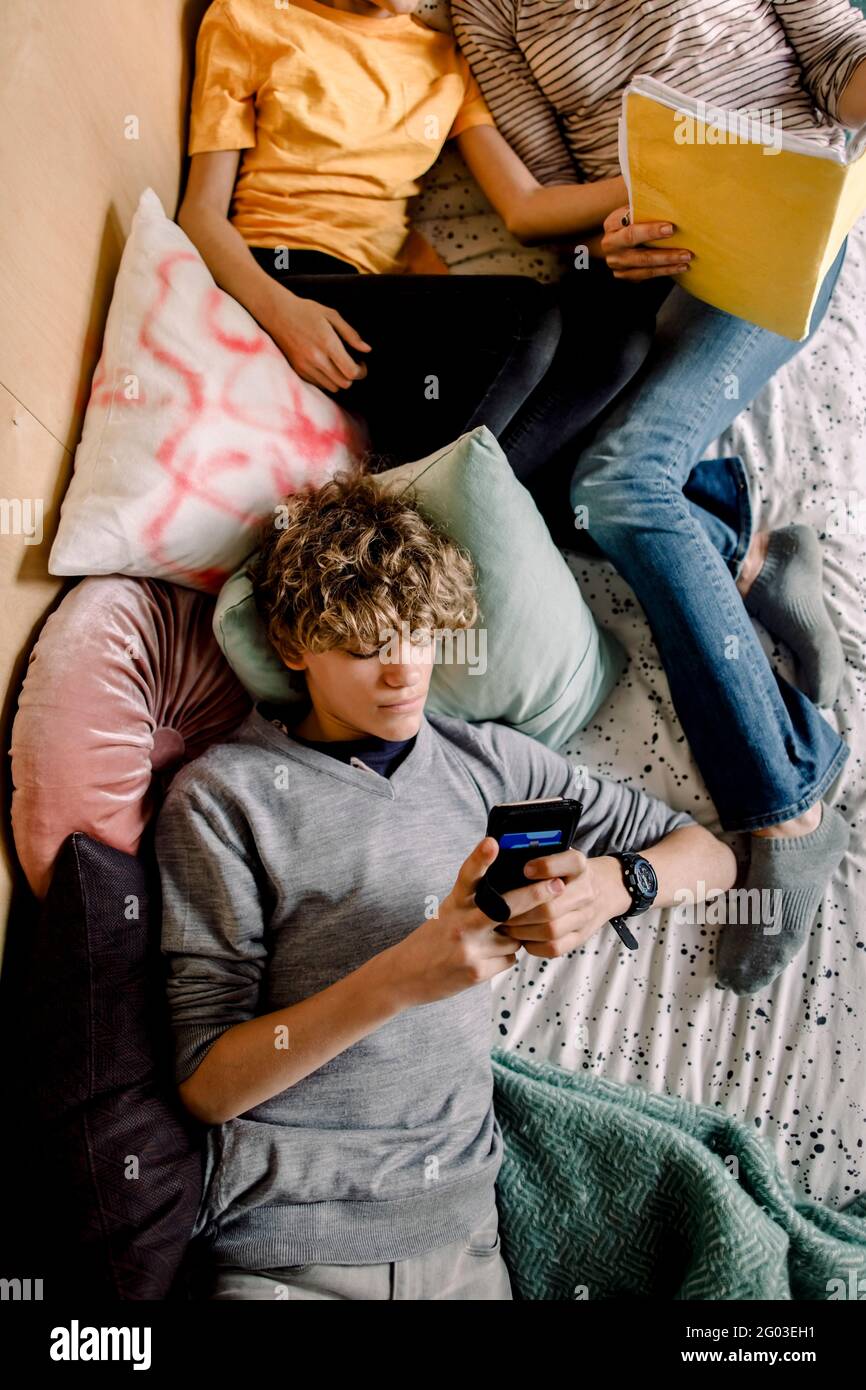 Boy using smart phone while lying in bedroom Stock Photo