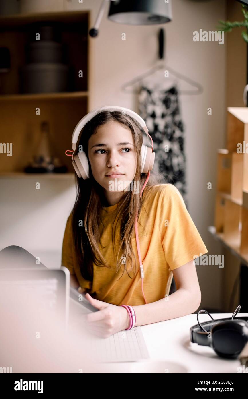 Girl wearing headphones sitting at desk while looking away Stock Photo