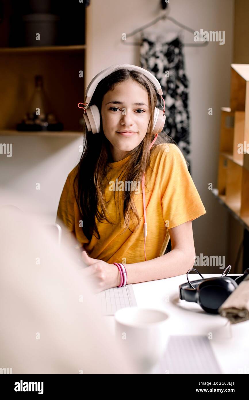 Portrait of smiling girl in yellow T-shirt sitting at desk Stock Photo