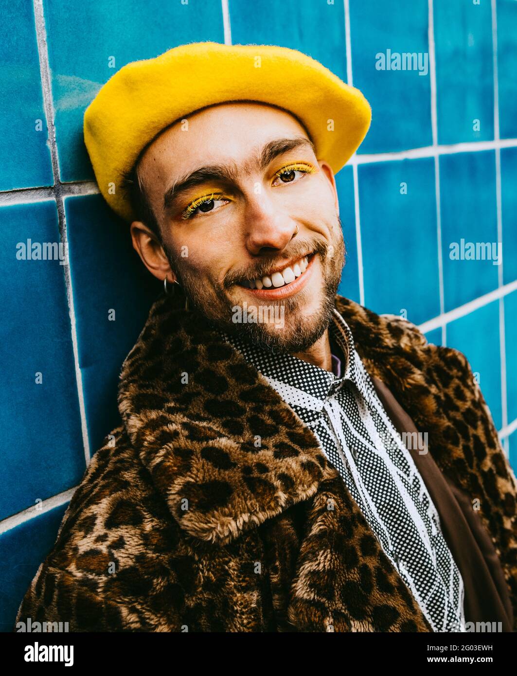 Portrait of smiling young man wearing yellow beret against blue tiled ...