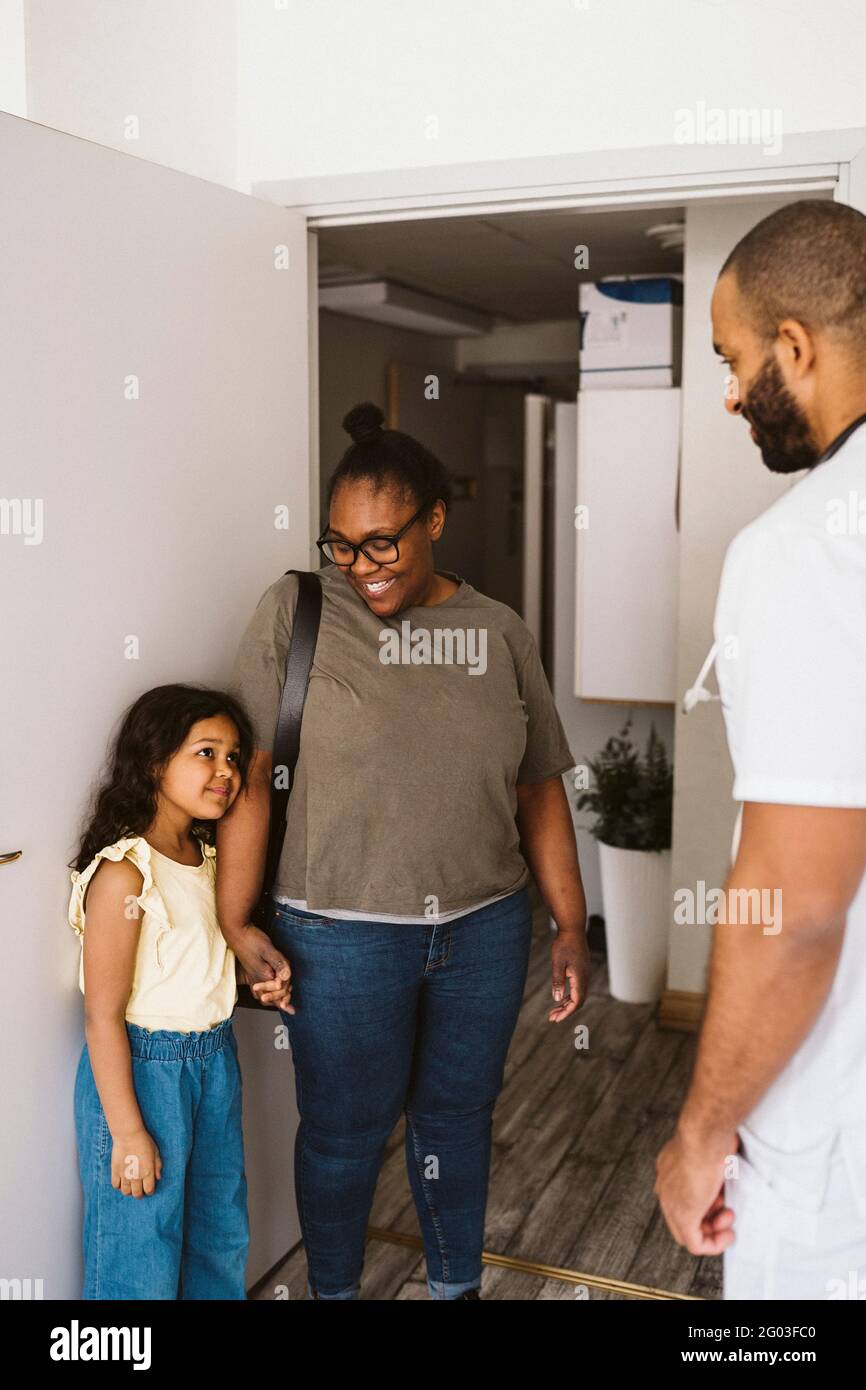 Girl looking at male pediatrician while standing by mother at medical clinic doorway Stock Photo