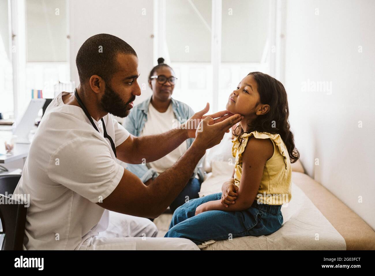 Male doctor examining throat of girl while sitting in medical clinic Stock Photo