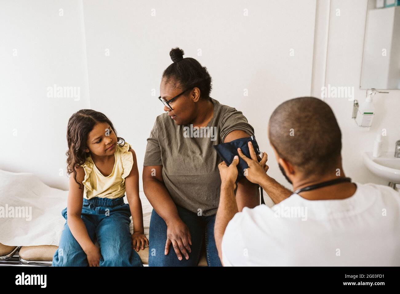 Mother talking with daughter while male doctor measuring blood pressure Stock Photo