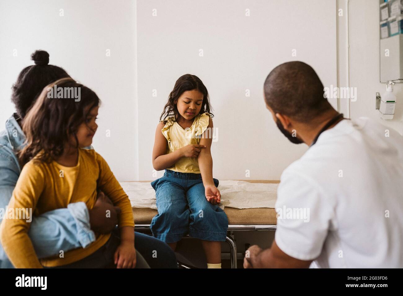 Girl talking with male doctor while pointing at hand in medical clinic Stock Photo