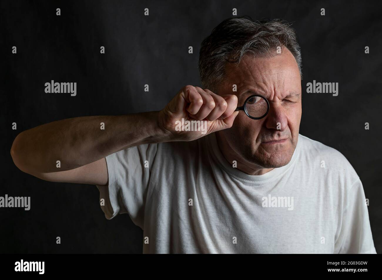 A man holds a magnifying glass in front of one eye looking through it with a very funny expression Stock Photo