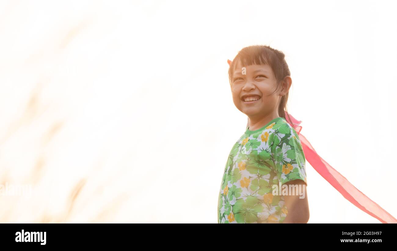 Asian little child girl is holding and smiling with a kite on meadow in summer in nature Stock Photo