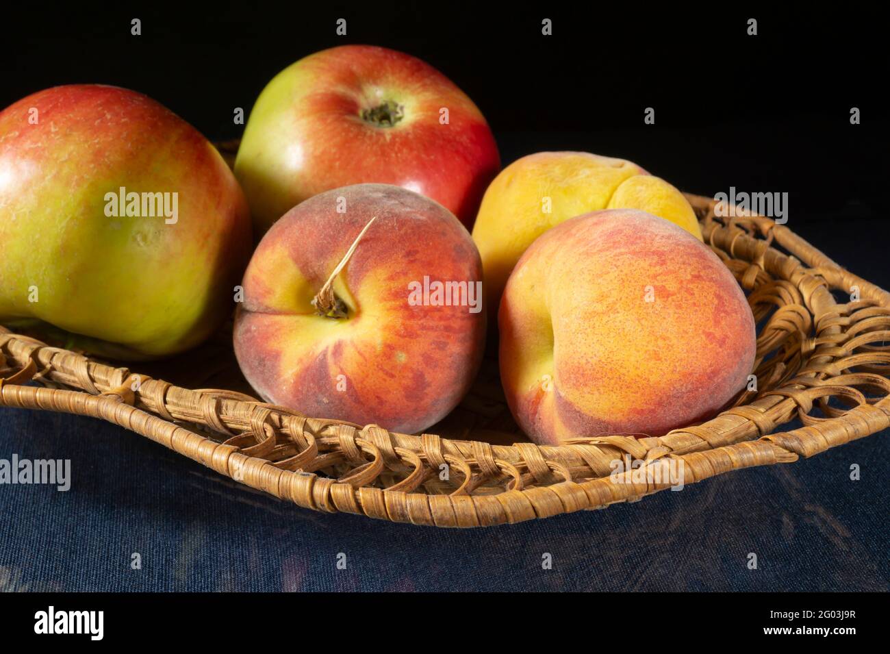Peaches and apples in a basket on the table. Food on a black background Stock Photo