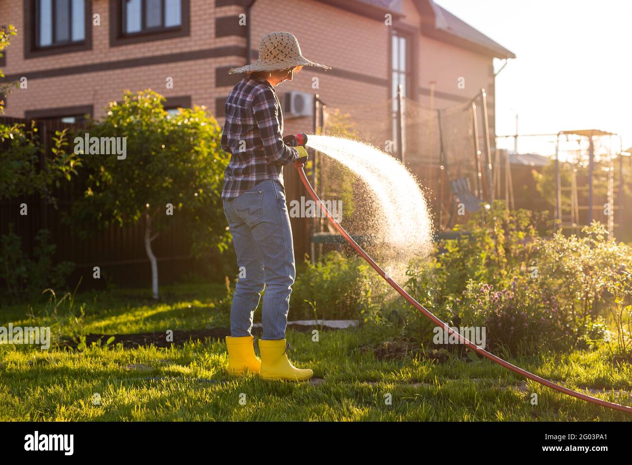 Woman holding garden water hose wearing colorful wellies watering garden Stock Photo