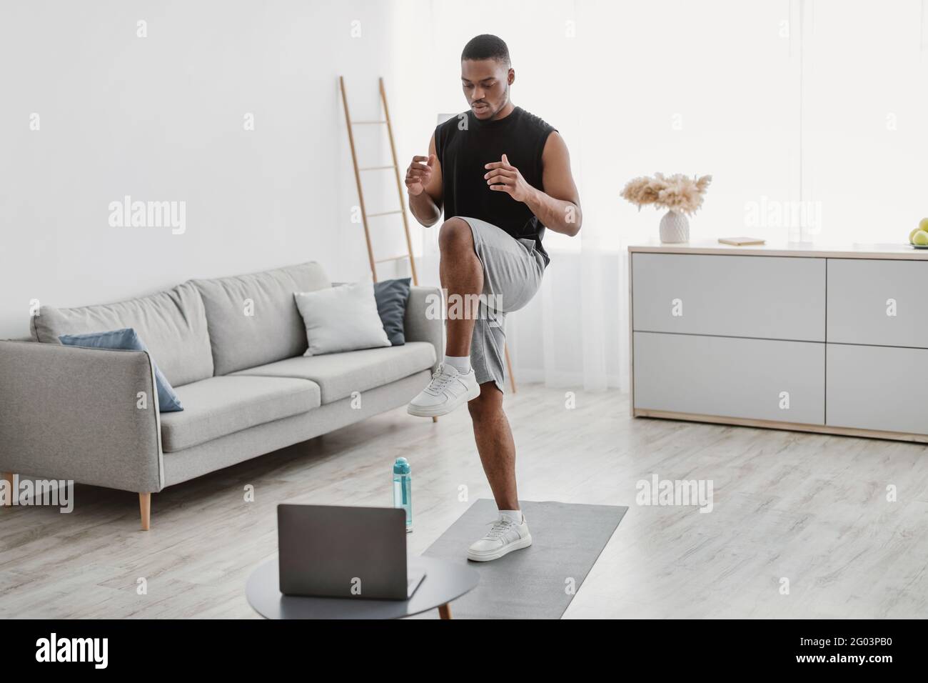 Black Man Doing Standing Knee Raise Exercise At Laptop Indoor Stock