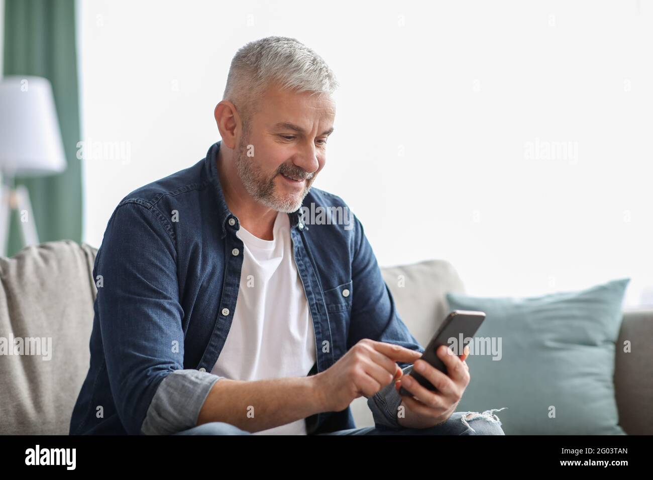 Smiling senior man using smartphone at home Stock Photo
