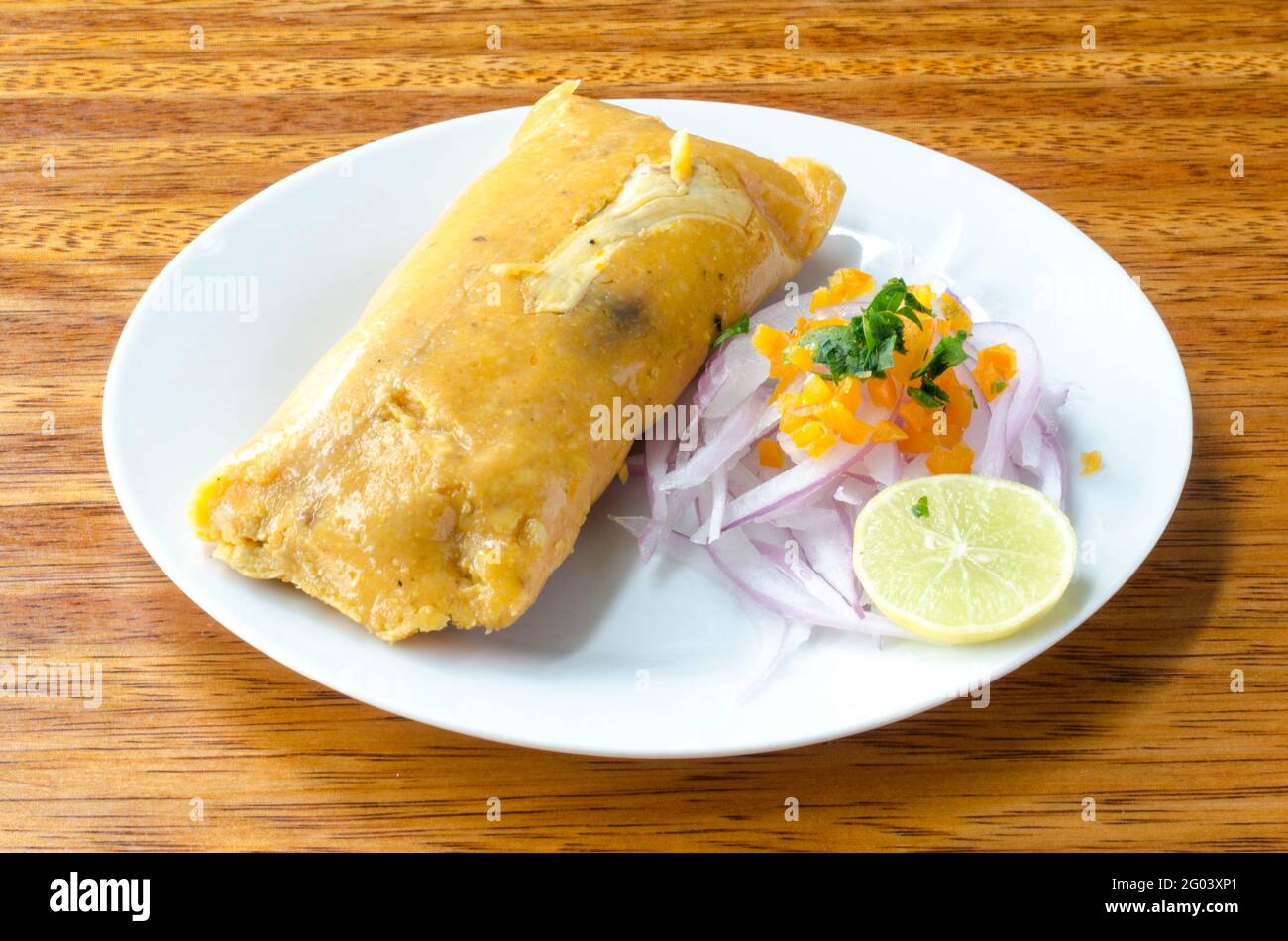 Peruvian tamale, traditionally eaten for breakfast on Sundays, made of corn and chicken and served with salsa criolla - onion salad. Stock Photo