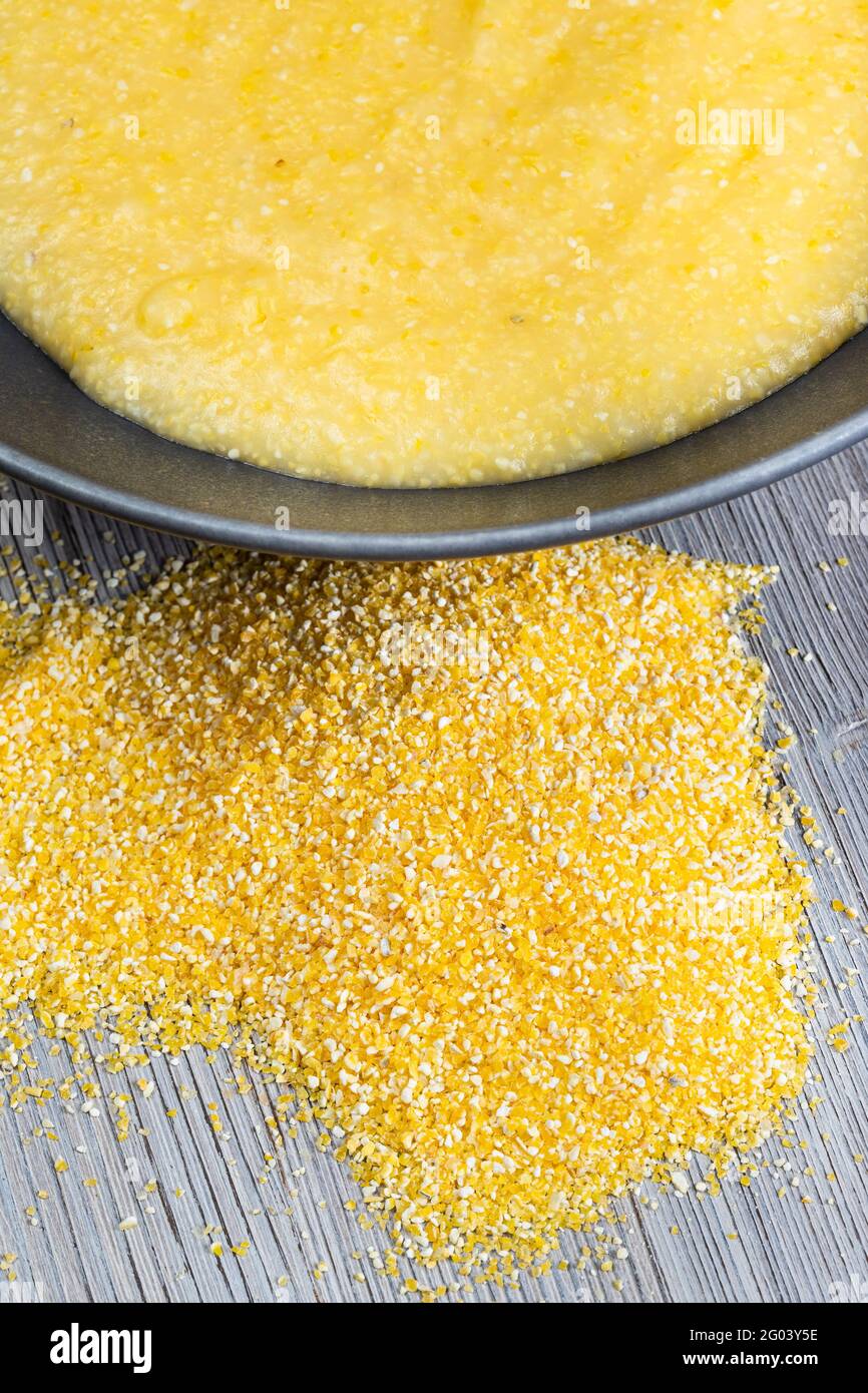 top view of handful of cornmeal and cooked maize porridge in gray bowl on gray wooden table Stock Photo