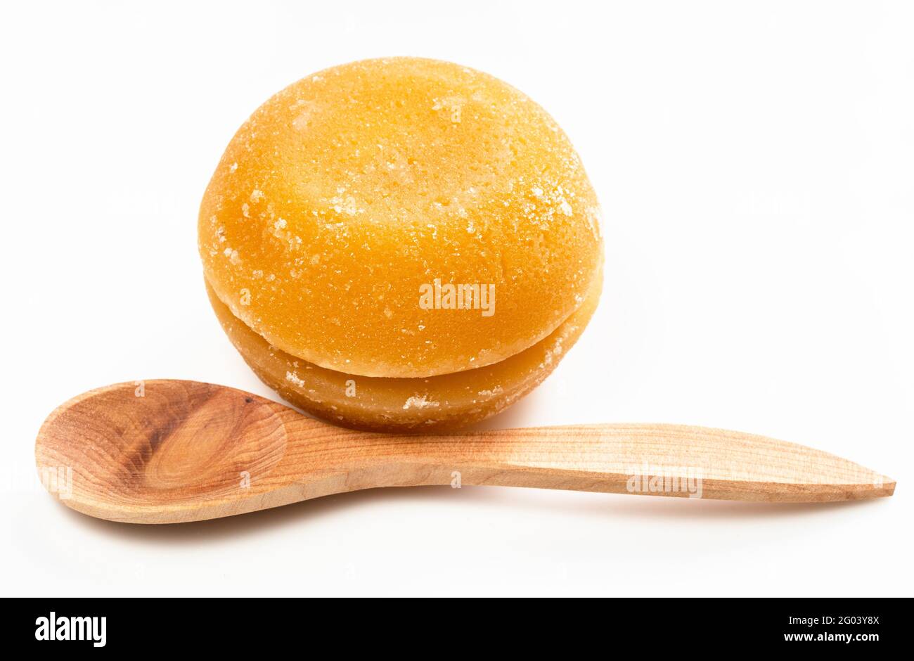 pair of whole round pieces of palm sugar near wooden spoon on gray ceramic plate Stock Photo