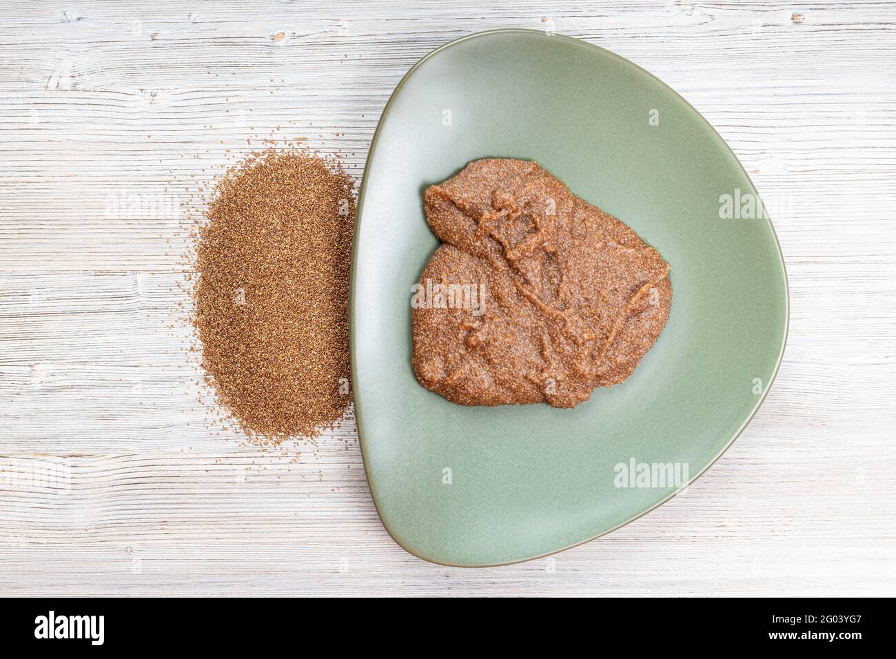 top view of teff grains and boiled porridge on green plate on wooden table Stock Photo