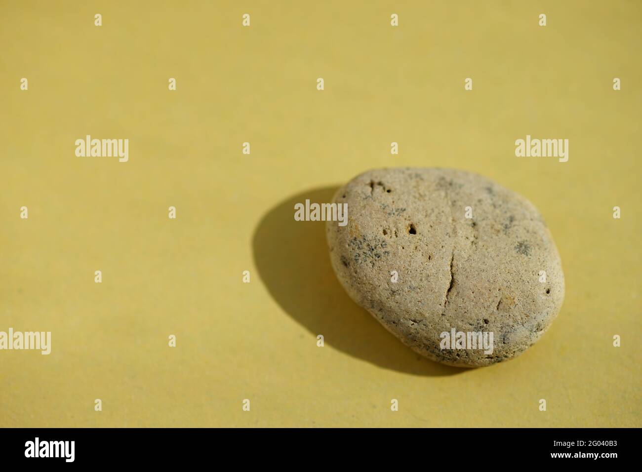 Beige pebble stone at yellow sunny table. Stock Photo