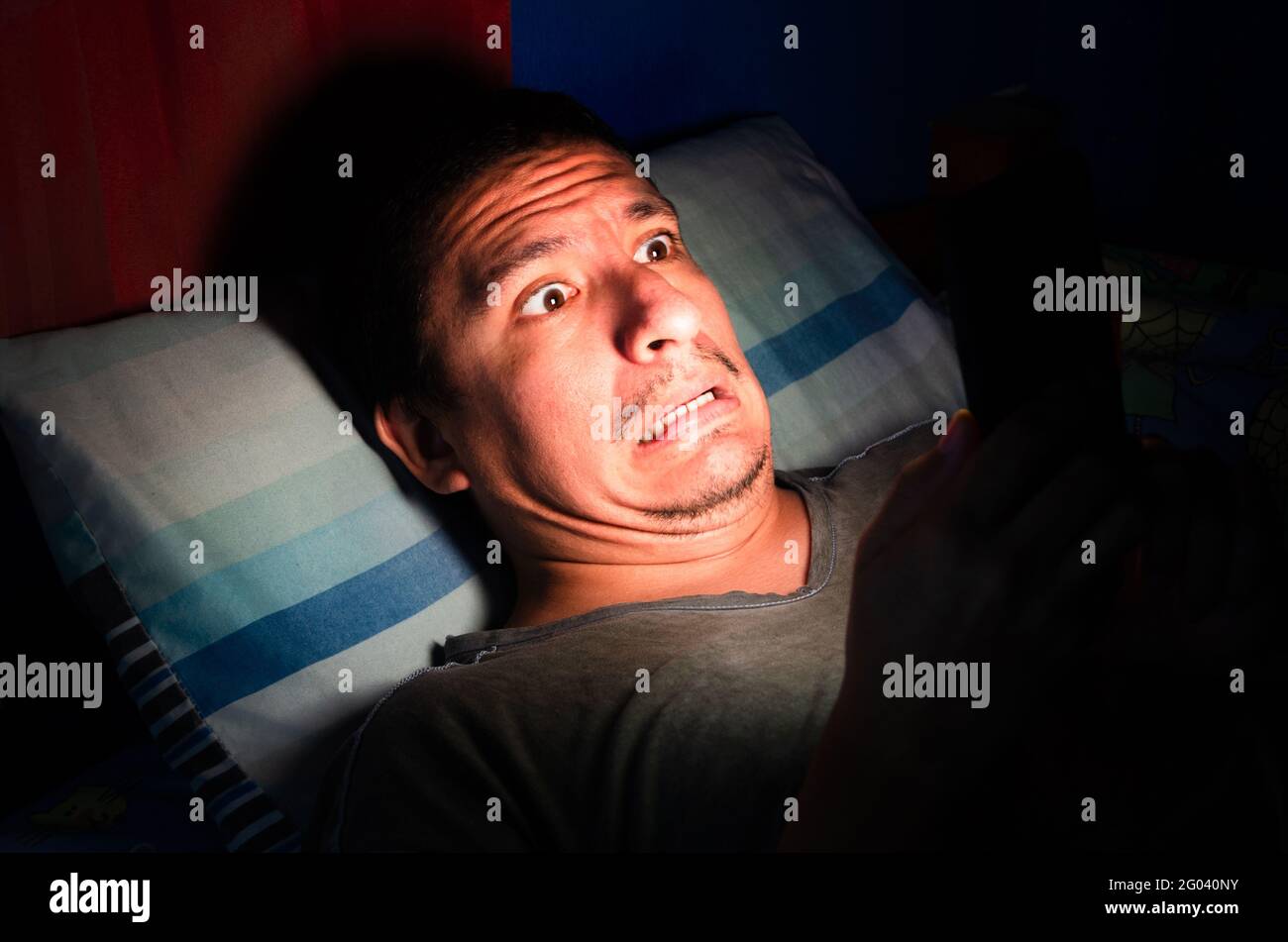 Anxious and awake man looks at his phone at night in the dark. Stock Photo
