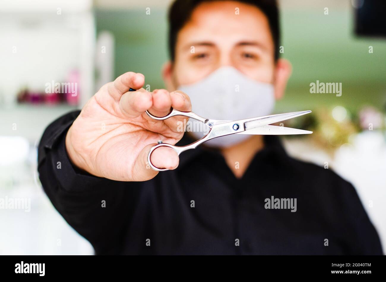 Portrait of an attractive barber, guy with safety mask, holding scissors in his hand, social distancing, preventive measures against the virus in Stock Photo