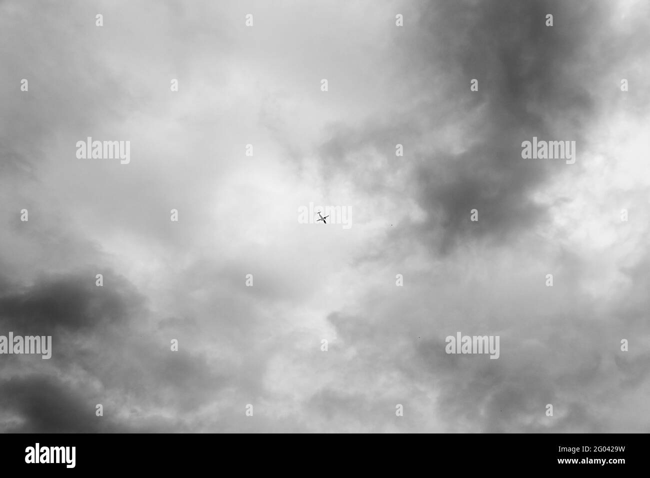 Black and white photo, bottom view of a passenger plane taking off or landing against a bright blue sky. Aerospace industry or tourism industry. Stock Photo