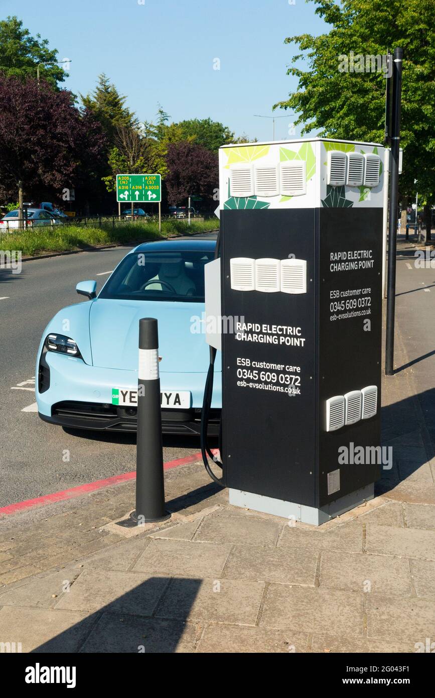 Porche luxury performance EV / E V car vehicle; batteries being charged up after running low on power, using an electrical cable from a Rapid Electric Charging Point at the side of a busy main road, the A316 in West London. UK. (123) Stock Photo
