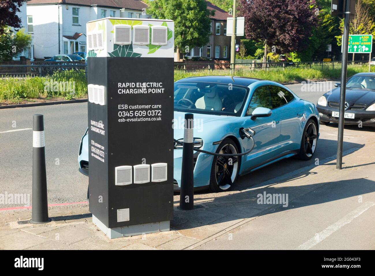 Porche luxury performance EV / E V car vehicle; batteries being charged up after running low on power, using an electrical cable from a Rapid Electric Charging Point at the side of a busy main road, the A316 in West London. UK. (123) Stock Photo