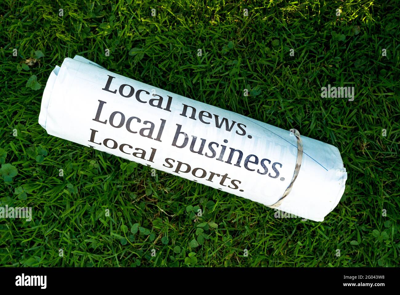 Morning paper rolled up and secured with an elastic laying on the lawn. Stock Photo