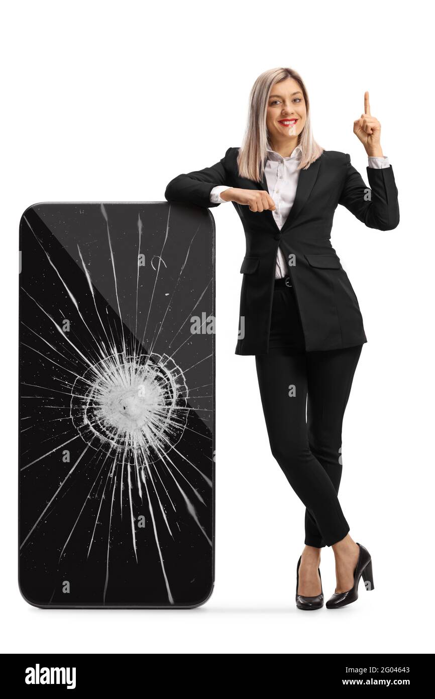 Full length portrait of a professional woman leaning on a smartphone with cracked screen and pointing up isolated on white background Stock Photo