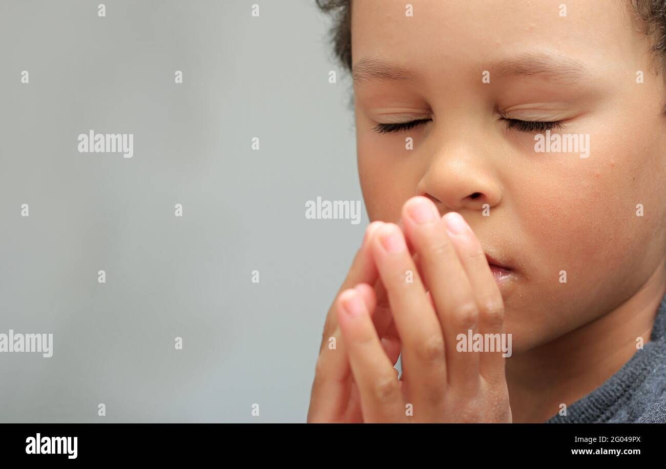 boy praying to god with closed eyes and hands held together stock photo