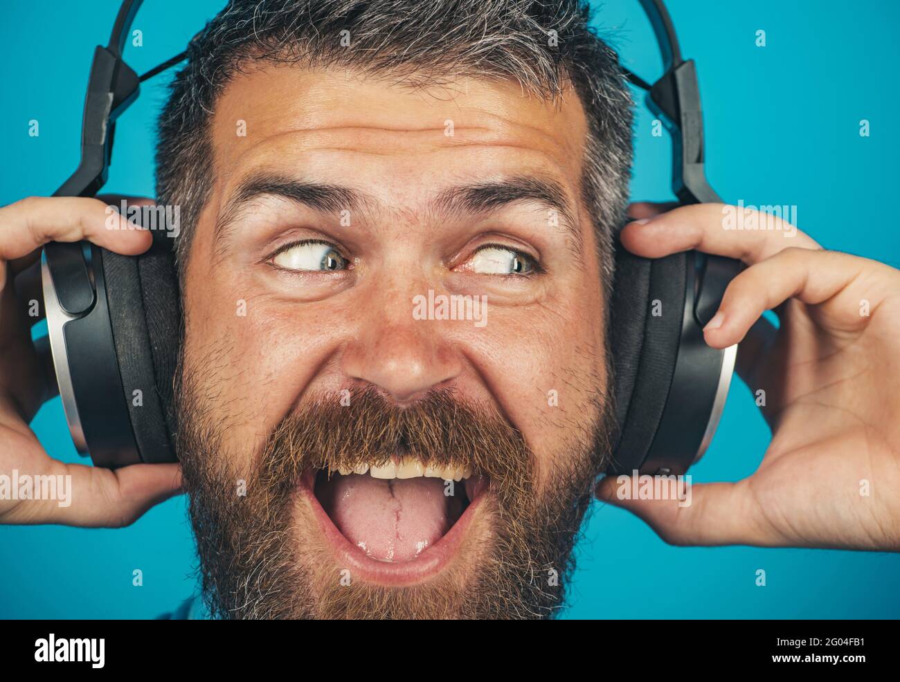 Handsome smiling bearded man with headphones. Emotional male with headphone listening music. Stock Photo
