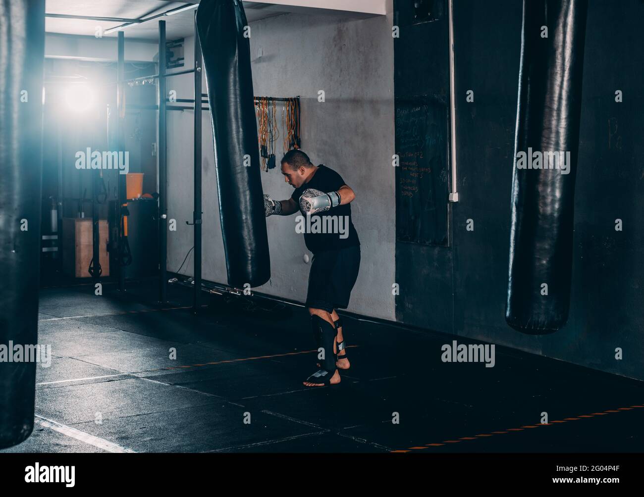 Young muscle boxer using a punching bag in gym. Boxer hitting punching