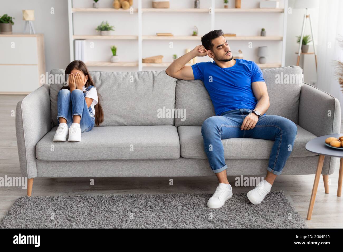 Father sitting separate on couch with offended crying daughter Stock Photo