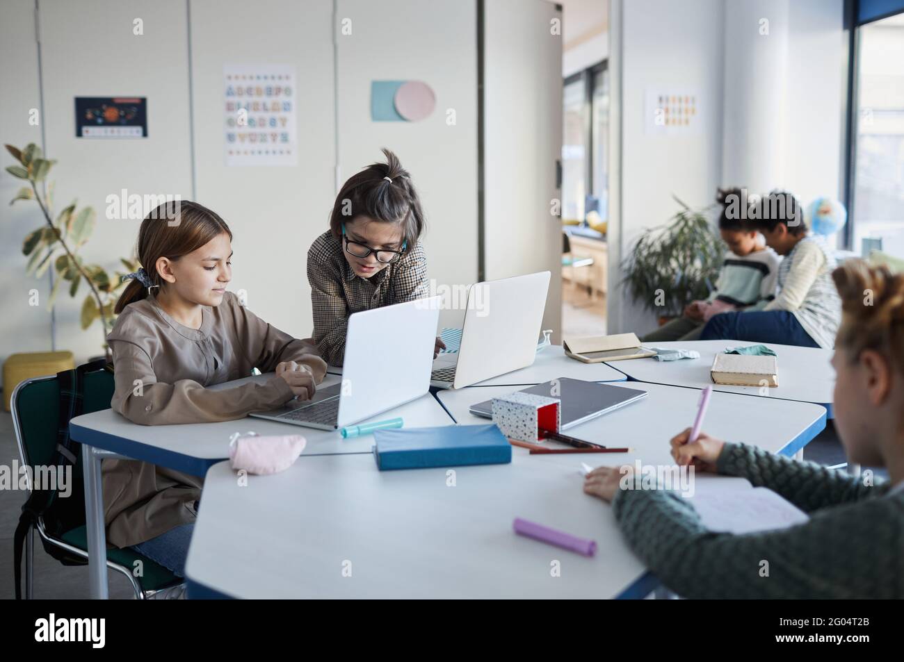 Diverse group of children working together at desk in classroom at modern school, copy space Stock Photo