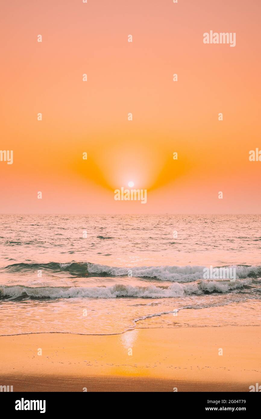 Sunset Sun Shine Above Sea. Natural Sunrise Sky Warm Colors Over Ripple Sea. Ocean Water Foam Splashes Washing Sandy Beach Stock Photo