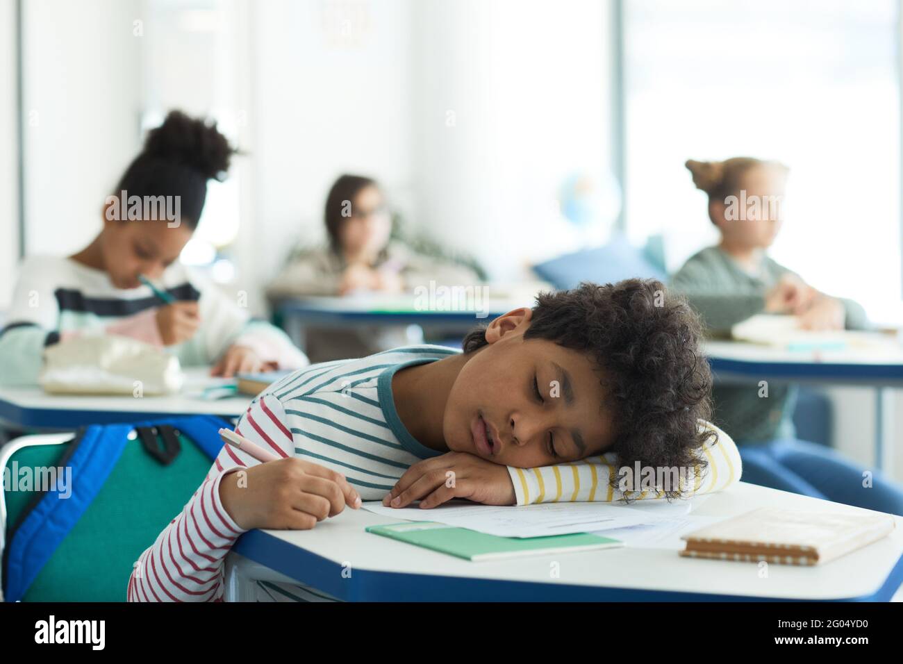 Portrait of mixed-raced boy sleeping at desk in school classroom, copy space Stock Photo
