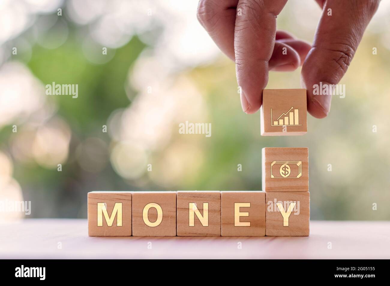 A hand holding a square wooden block with graph icons with MONEY messages. Ideas for financial and business growth. Stock Photo
