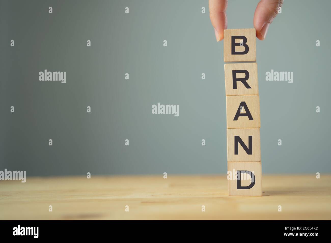 The hand put text Brand on wooden block on wooden table with gray background. Target of building brand concept, improve brand, strengthen brand, brand Stock Photo