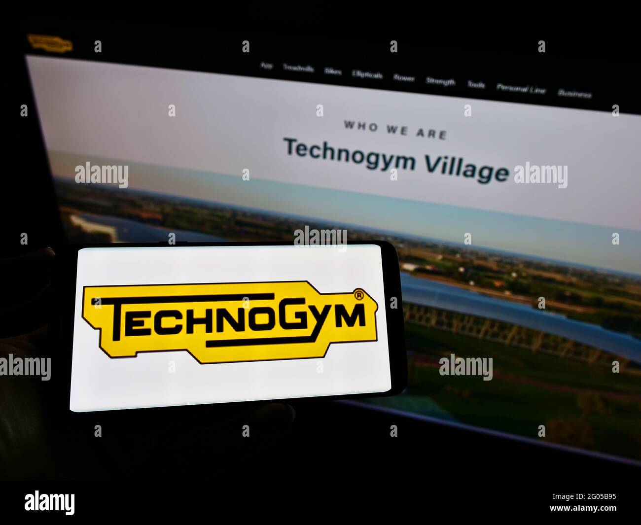 Person holding mobile phone with logo of Italian fitness equipment company Technogym S.p.A. on screen in front of web page. Focus on phone display. Stock Photo