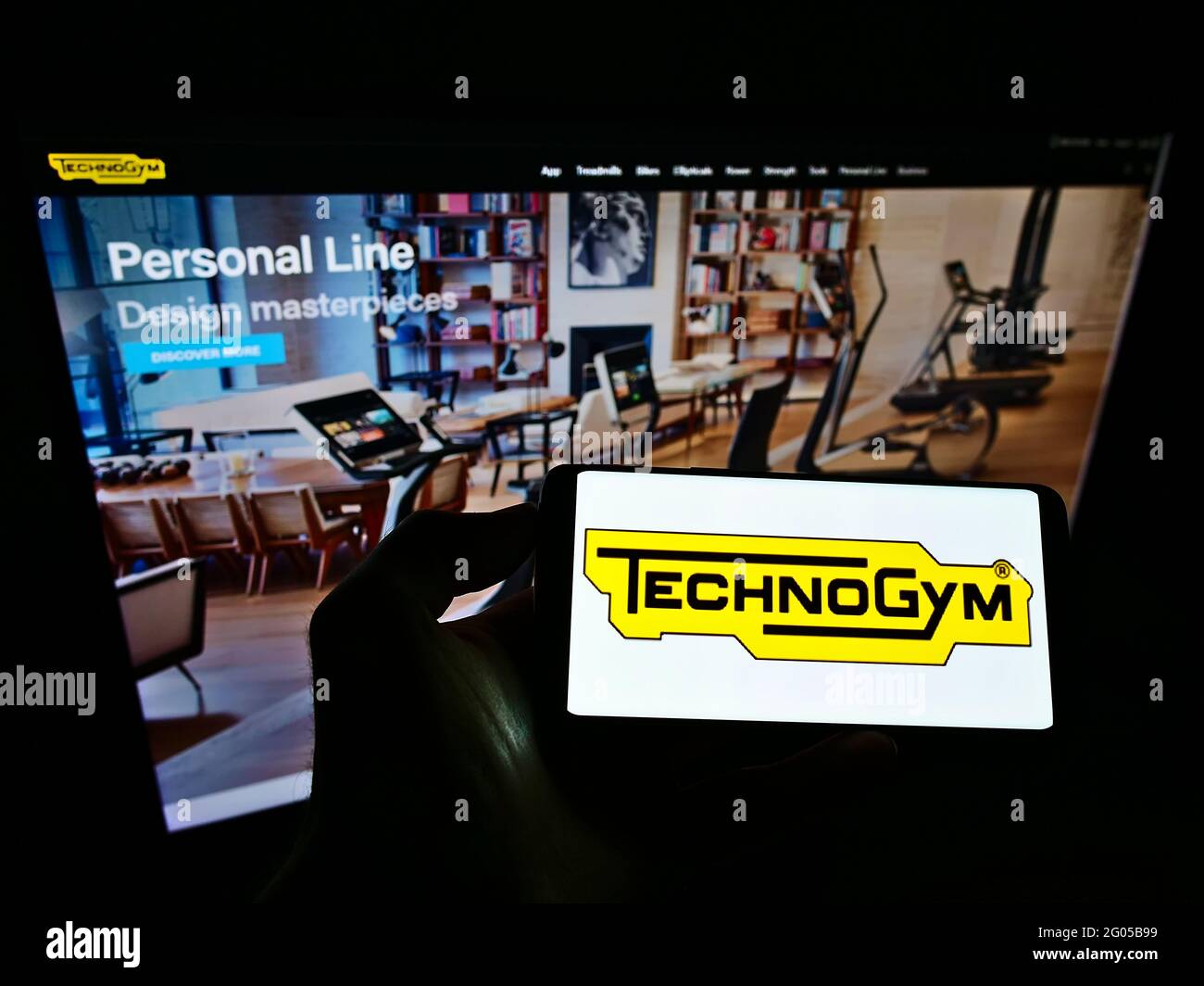 Person holding cellphone with logo of Italian fitness equipment company Technogym SpA on screen in front of business website. Focus on phone display. Stock Photo