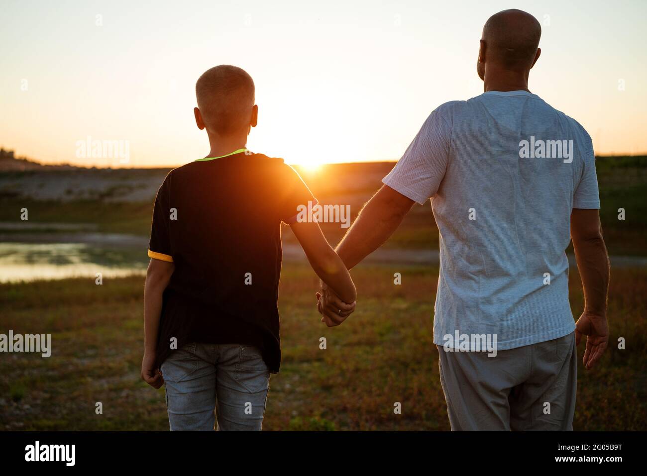 Son and dad stand against the backdrop of a colorful sunset. The