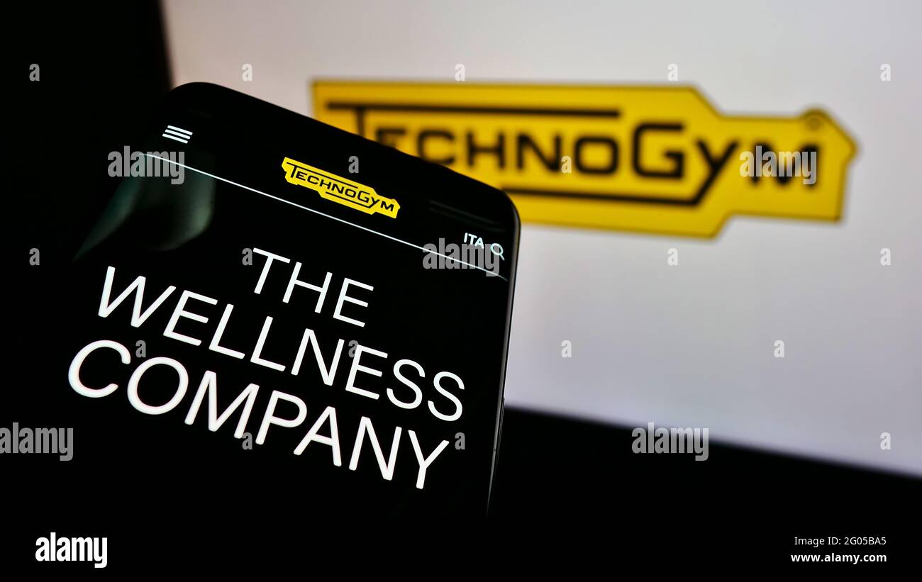 Mobile phone with website of Italian fitness equipment company Technogym SpA on screen in front of business logo. Focus on top-left of phone display. Stock Photo