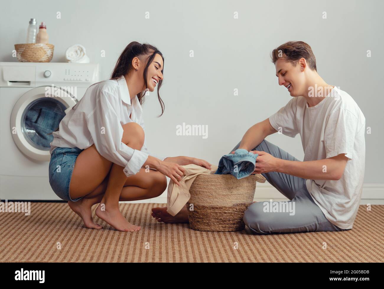 Beautiful young loving couple is smiling while doing laundry at home ...