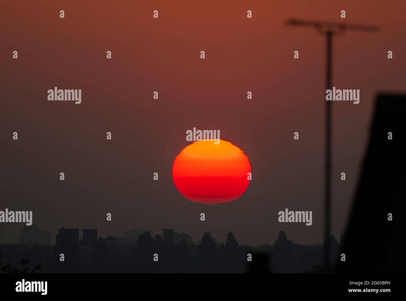 Wimbledon, London, UK. 1 June 2021. The rising sun contorts in shapes as it moves through thick layers of atmosphere near the horizon over London before it begins a day of mini heatwave temperatures. Credit: Malcolm Park/Alamy Live News. Stock Photo