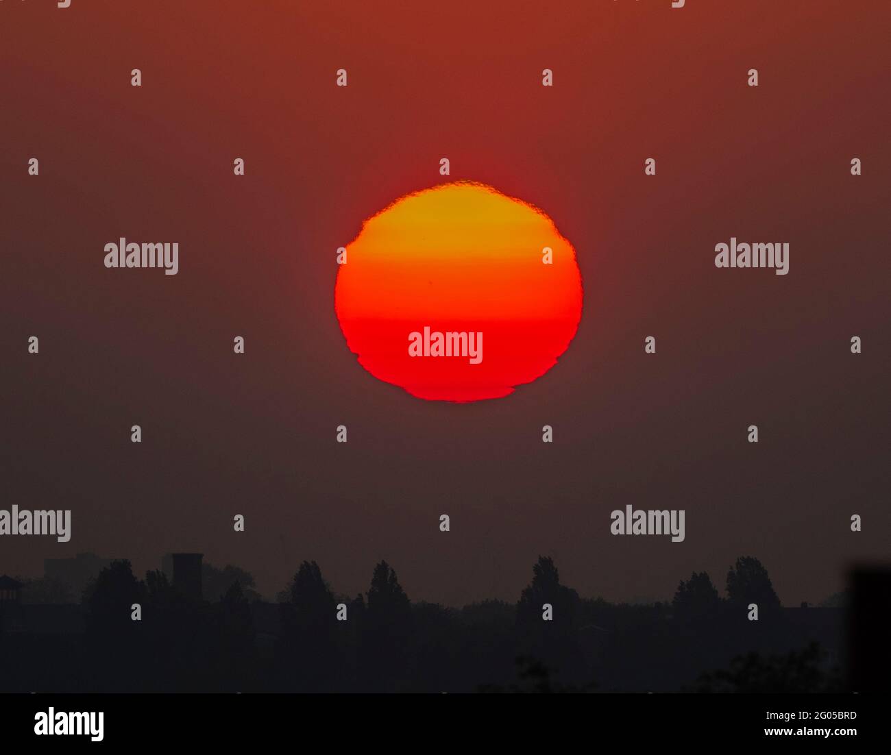 Wimbledon, London, UK. 1 June 2021. The rising sun contorts in shapes as it moves through thick layers of atmosphere near the horizon over London before it begins a day of mini heatwave temperatures. Credit: Malcolm Park/Alamy Live News. Stock Photo